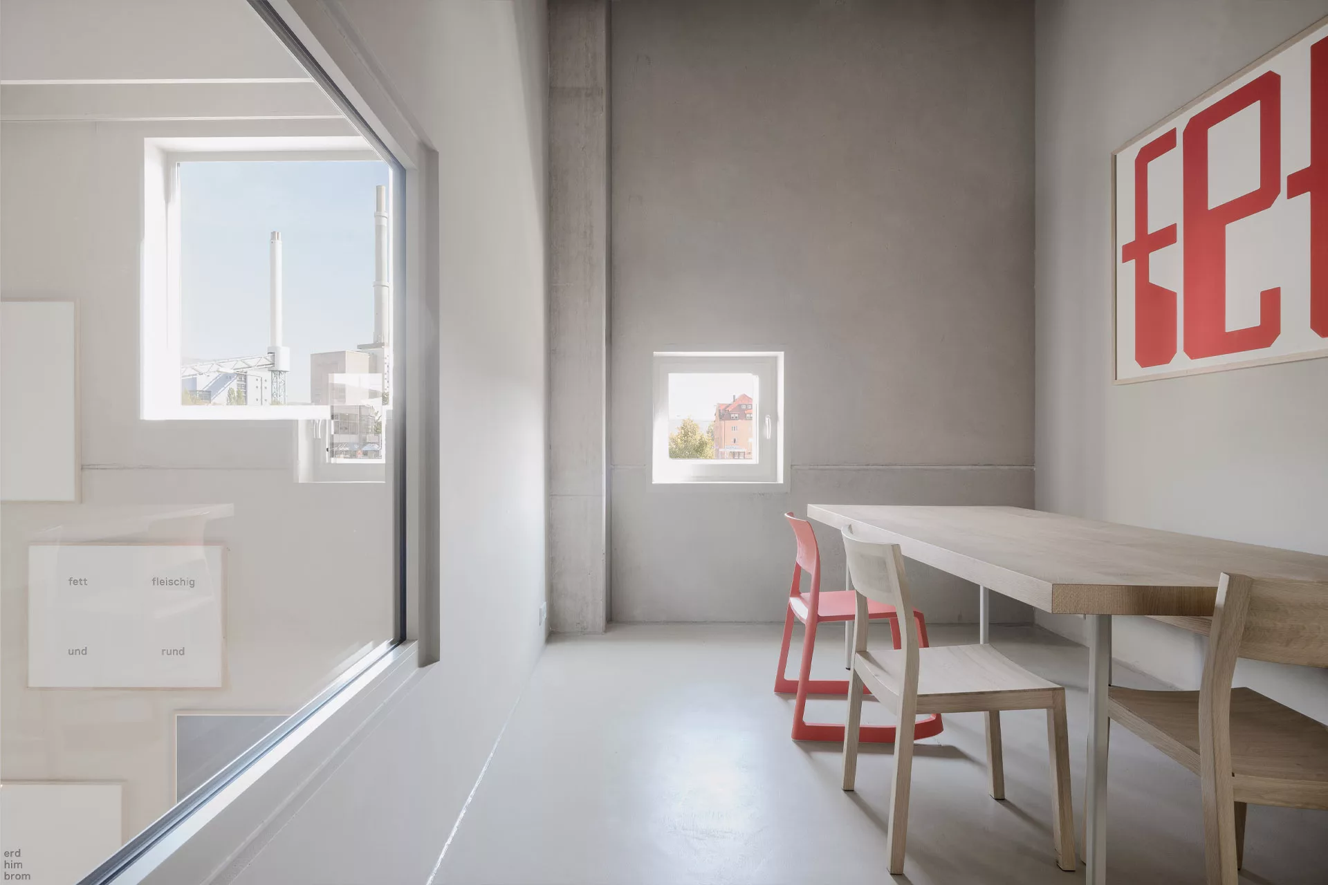 Minimalistisches Zimmer mit Holztisch, zwei Stühlen, einem Fenster mit Stadtblick und einem roten Kunstwerk an der Wand.