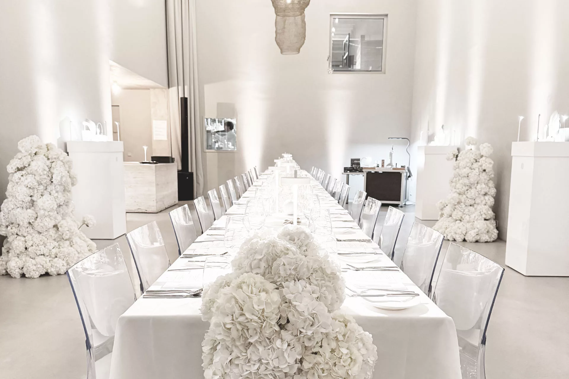 Elegante, lange Tafel mit weißen Tischdecken und Blumenarrangements in einem modernen, minimalistisch dekorierten Raum.