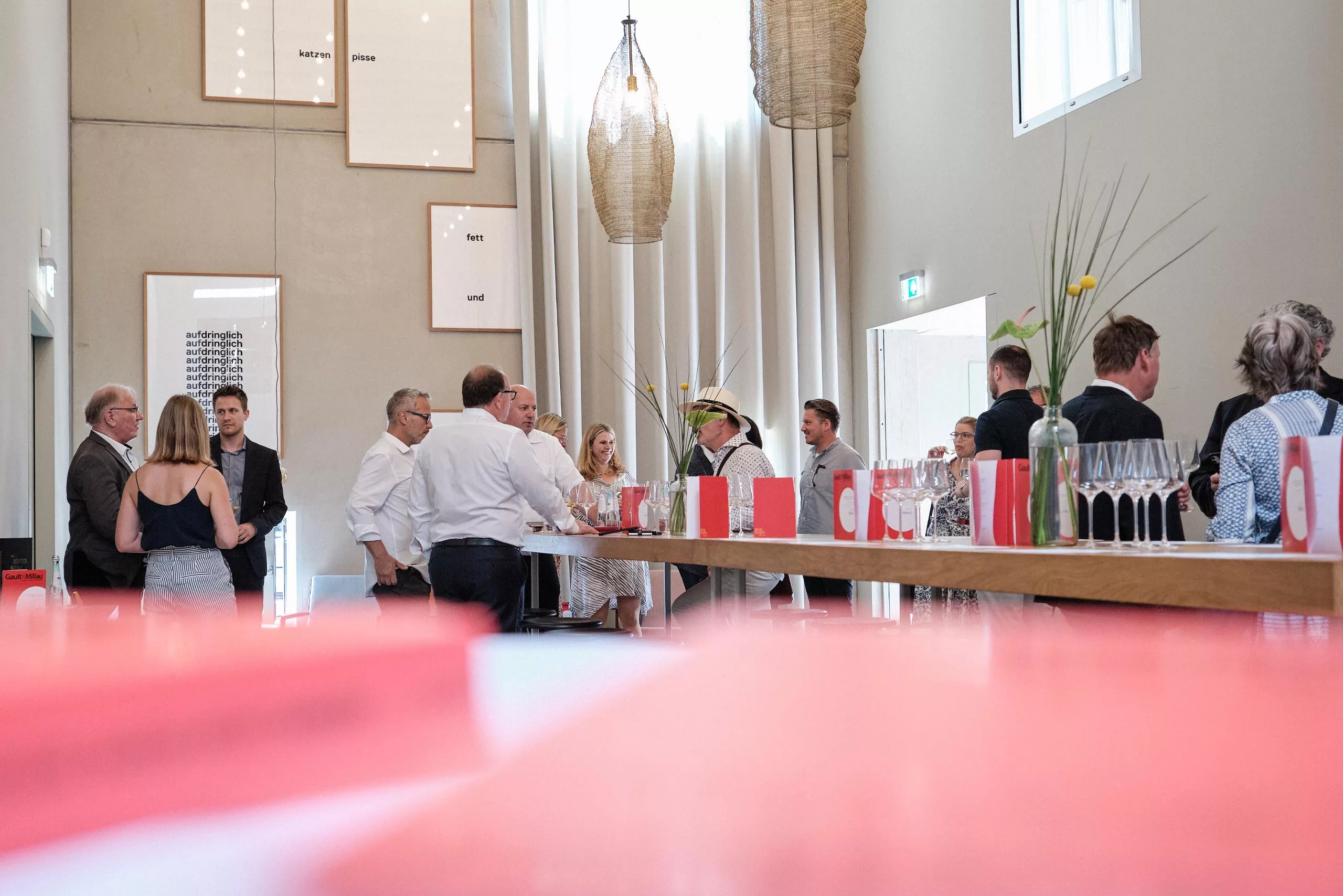Personengruppe in formeller Kleidung unterhält sich in modernem Raum mit hohen Decken und dekorativen Lampen.