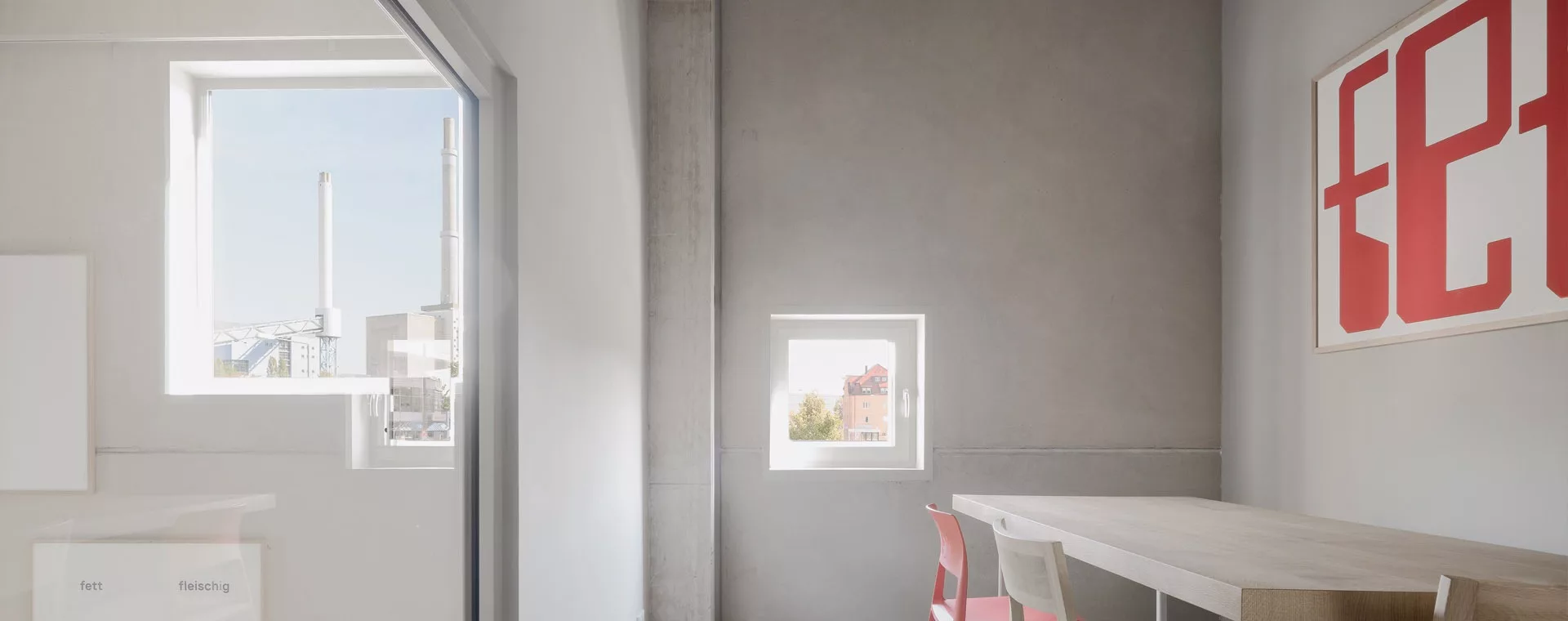 Modernes Zimmer mit Tisch und Stühlen, zwei Fenstern mit Ausblick, und einem großen, rot-weißen Kunstwerk an der Wand.