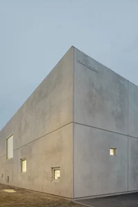 Modernes Betongebäude mit kleinen Fenstern und glatter Oberfläche bei Tagesanbruch.